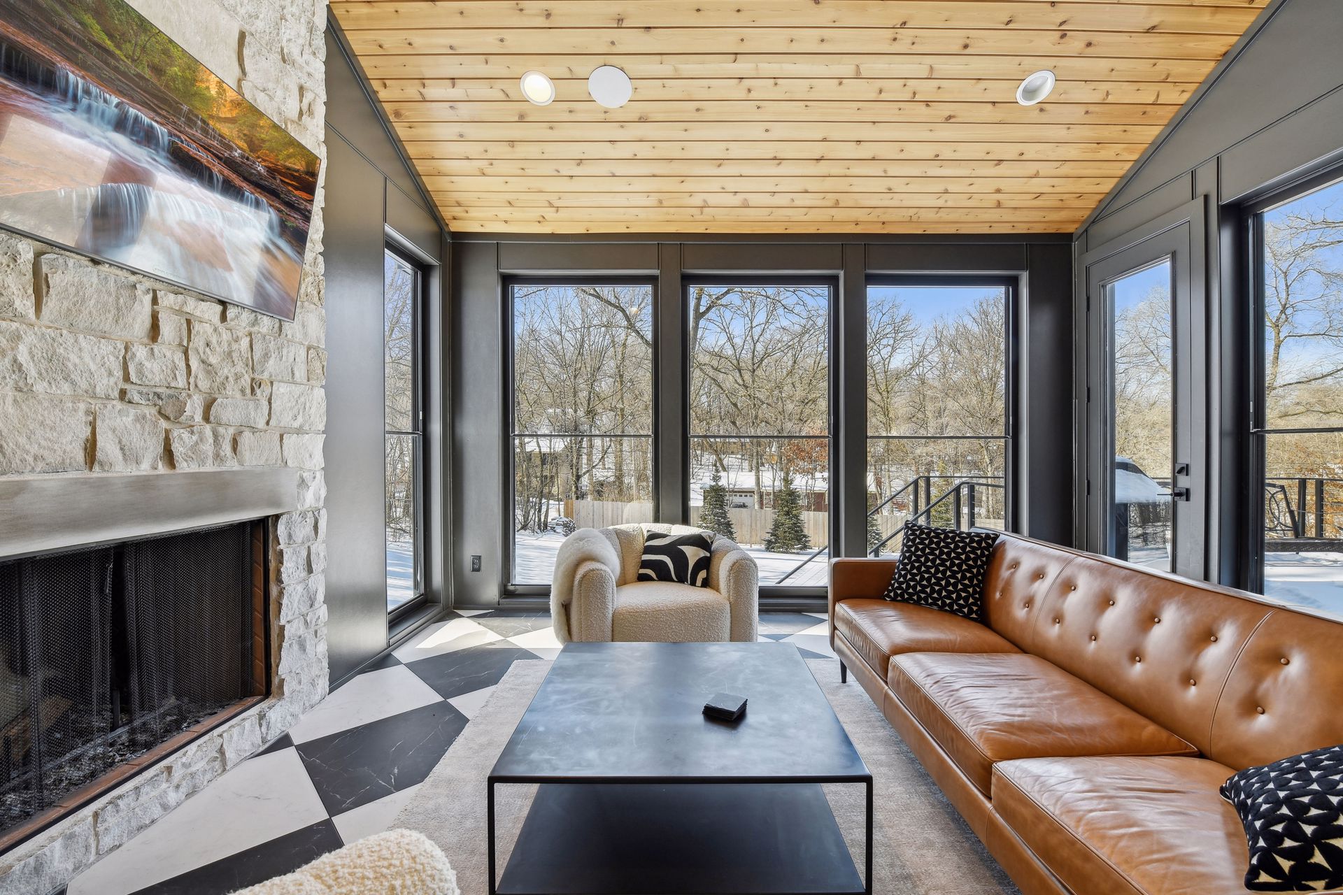 Four-season porch with cedar ceiling, stone fireplace and leather sofa